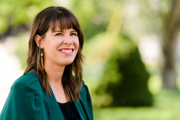 A woman wearing a green jacket poses for a picture outdoors.